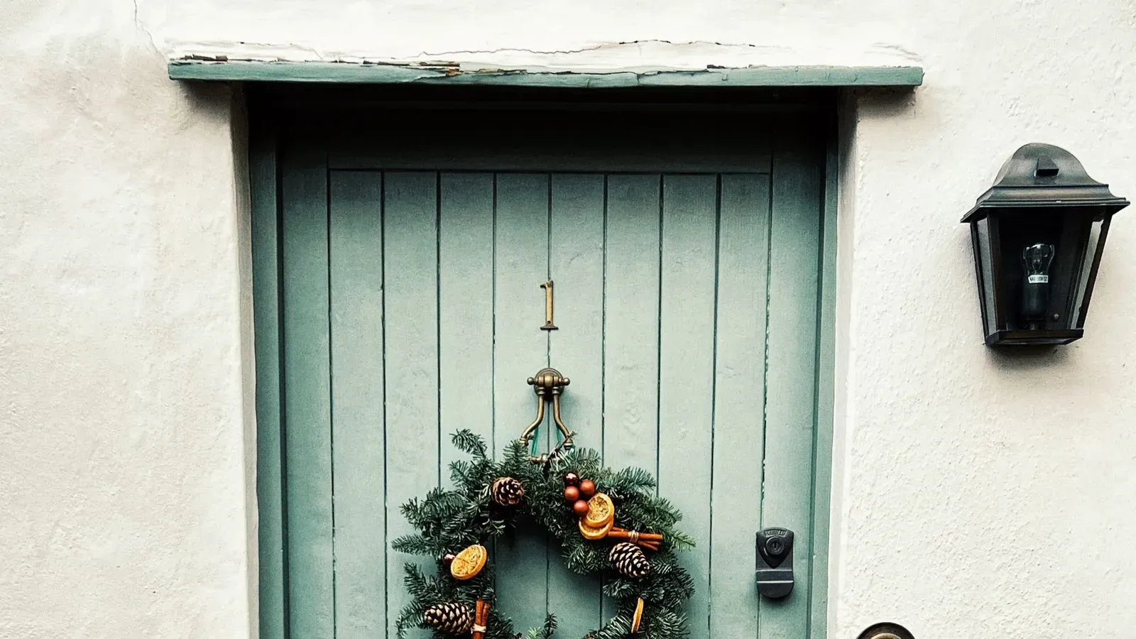 Christmas wreath with orange slices and a gold bow on a sage green cottage door with flower pots