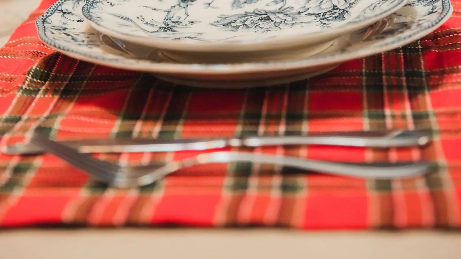 Red tartan table runner with a blue and white patterned plate and a softly lit Christmas tree behind