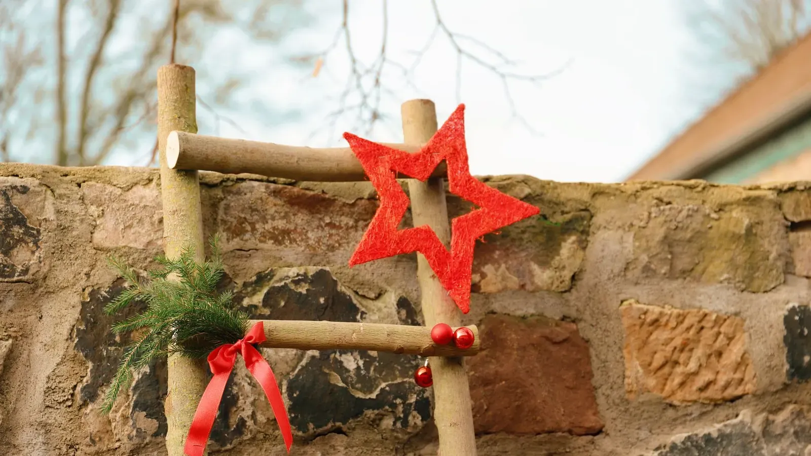 Rustic wooden ladder on a stone wall decorated with a red felt star, red ribbon bow and fir sprig