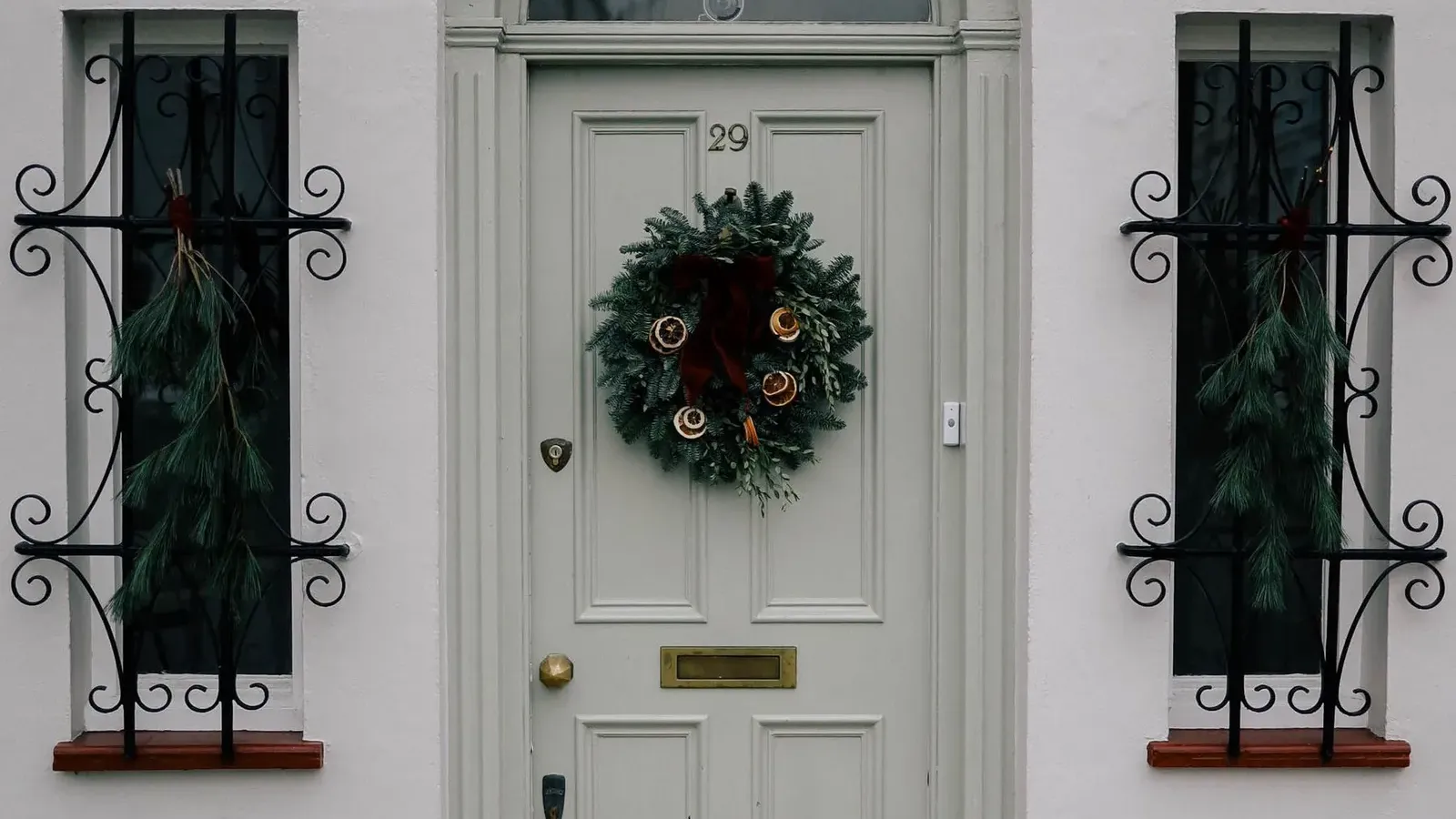 Christmas wreath on a pale grey panelled front door with an arched fanlight, flanked by windows with black iron grilles