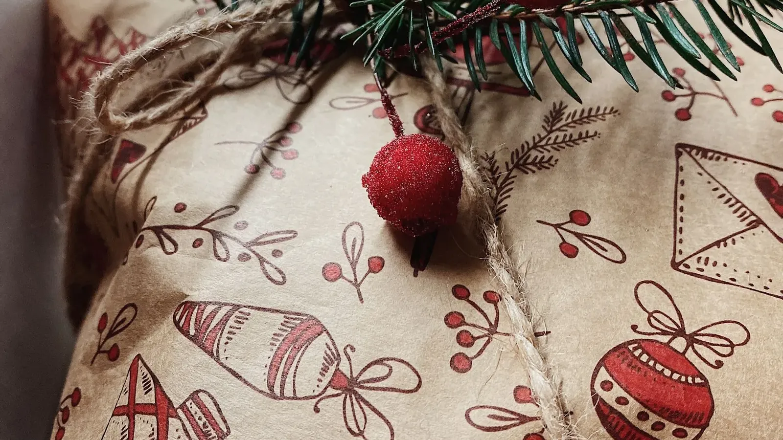 Close-up of a present in kraft paper with red festive drawings, tied with twine, a fir sprig and berries