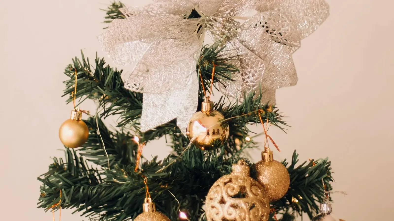 Gold glitter star topper above a white sheer bow and gold baubles on a fir tree, pale pink wall behind