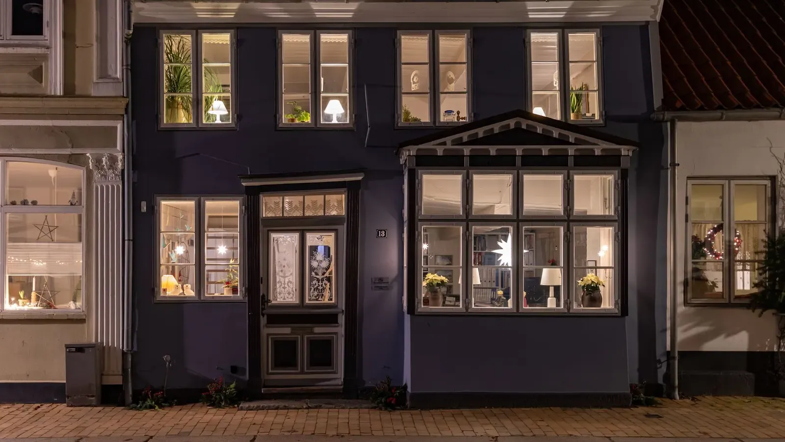 Blue-painted townhouse at night with warm glowing windows, paper stars and a glazed front door