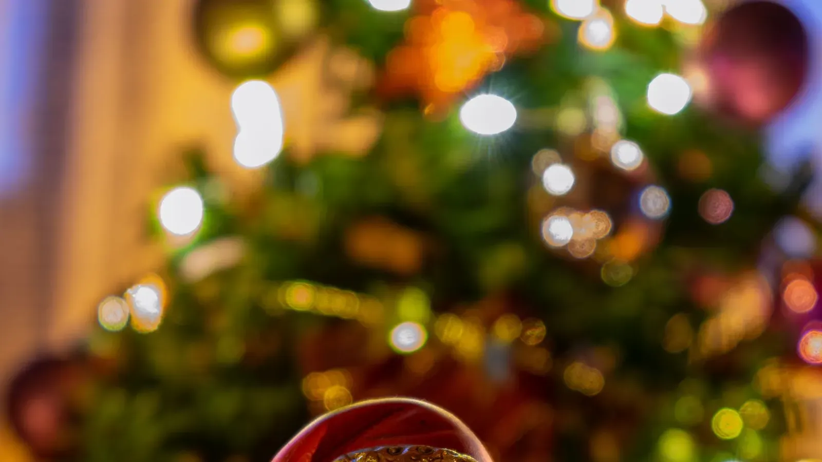 Golden ceramic Santa figure glowing warmly among fir branches and tree lights, with more lights blurred behind