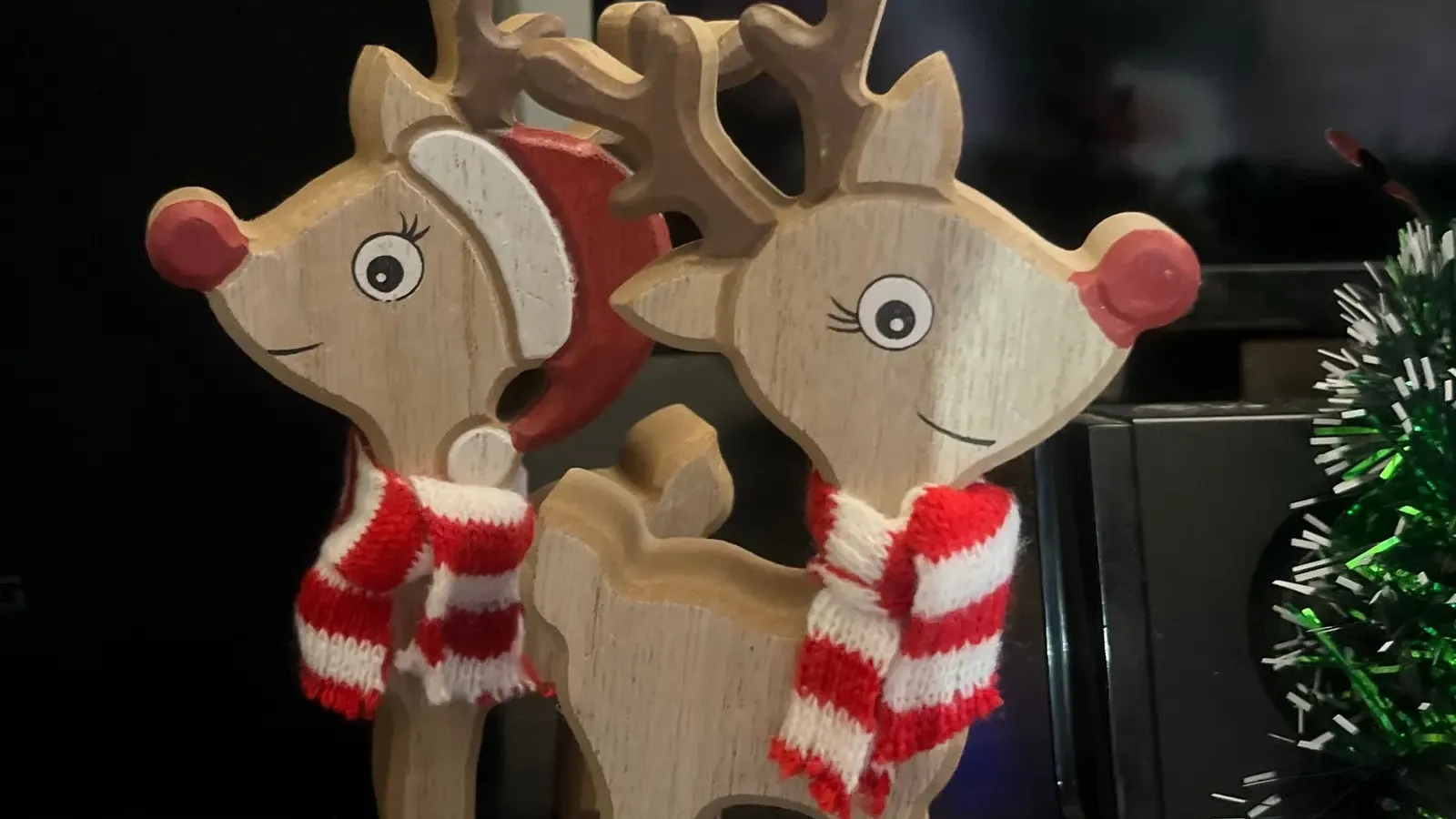 Pair of painted wooden reindeer figures wearing red and white striped scarves on a shelf beside tinsel