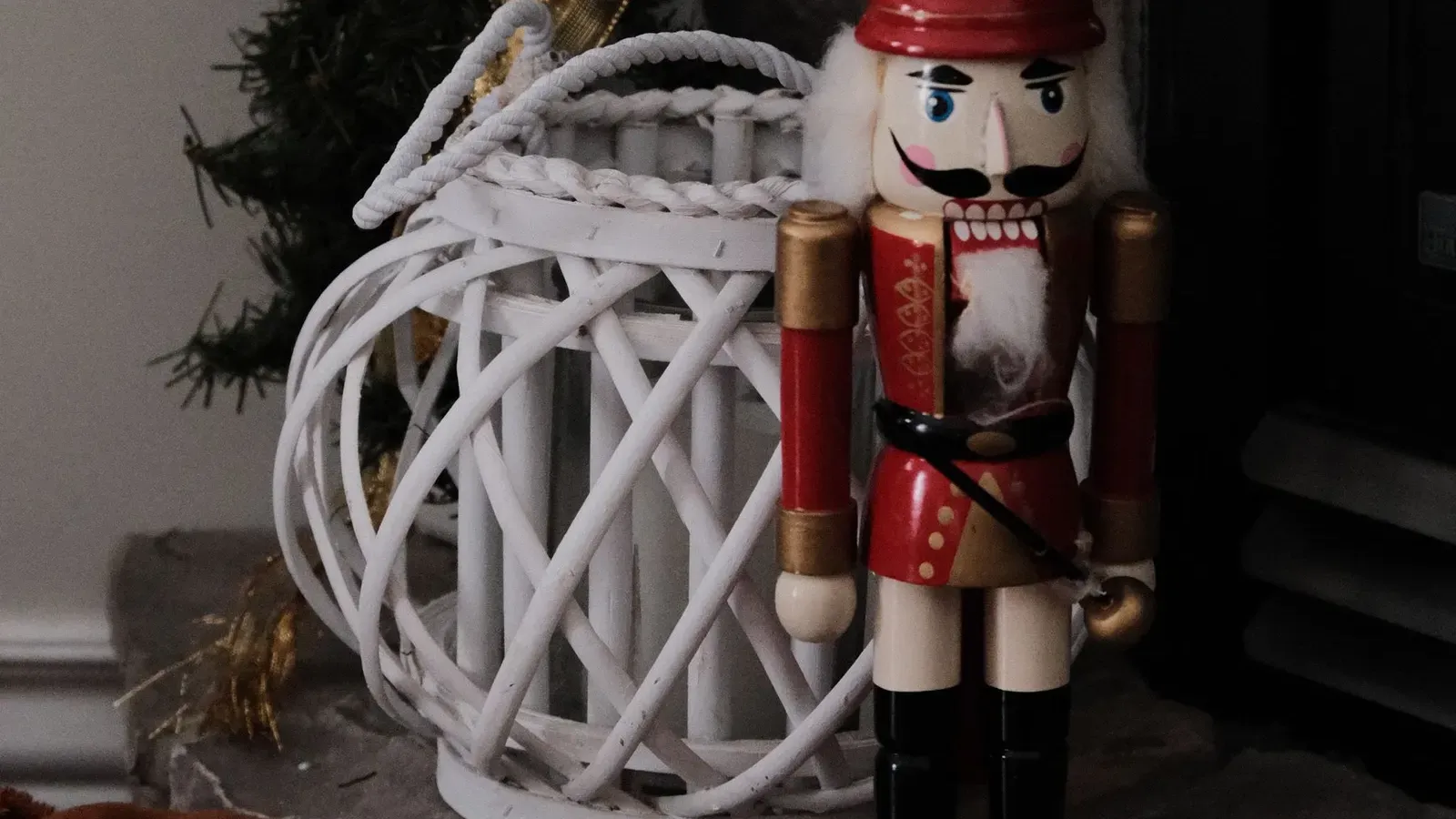 Red and cream wooden nutcracker beside a white wicker lantern and pine garland on a stone hearth