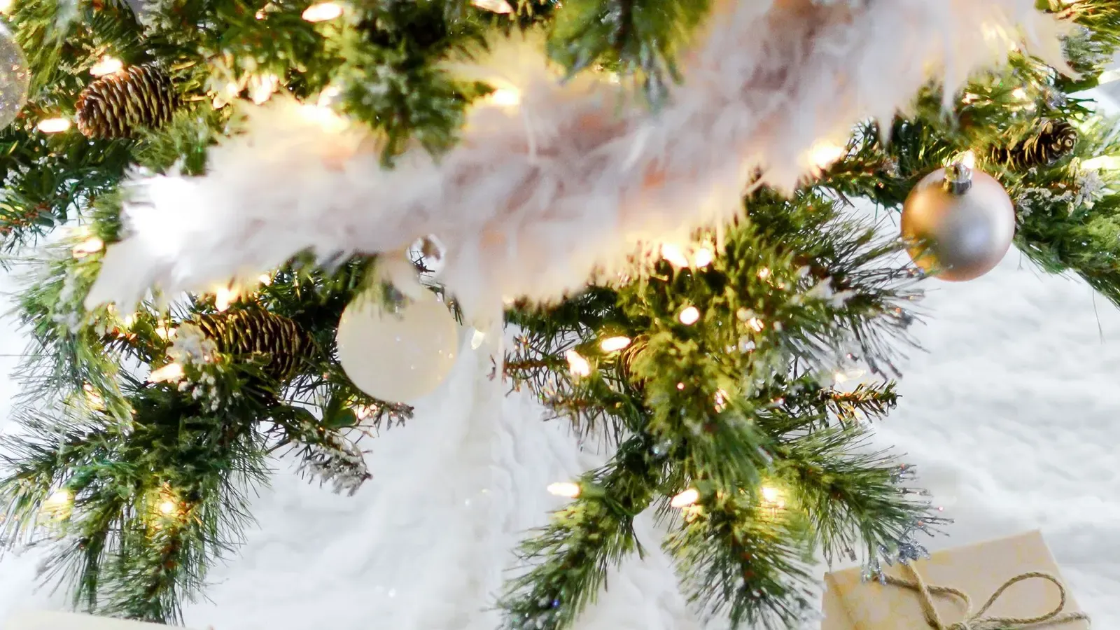 Gifts in pale gold paper tied with twine and fir sprigs on a white tree skirt, dark wooden floor
