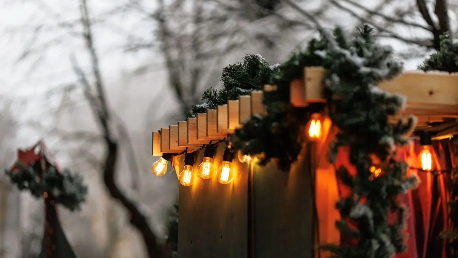 Market stall edged with a fir garland and vintage filament bulbs on a misty, frosty day