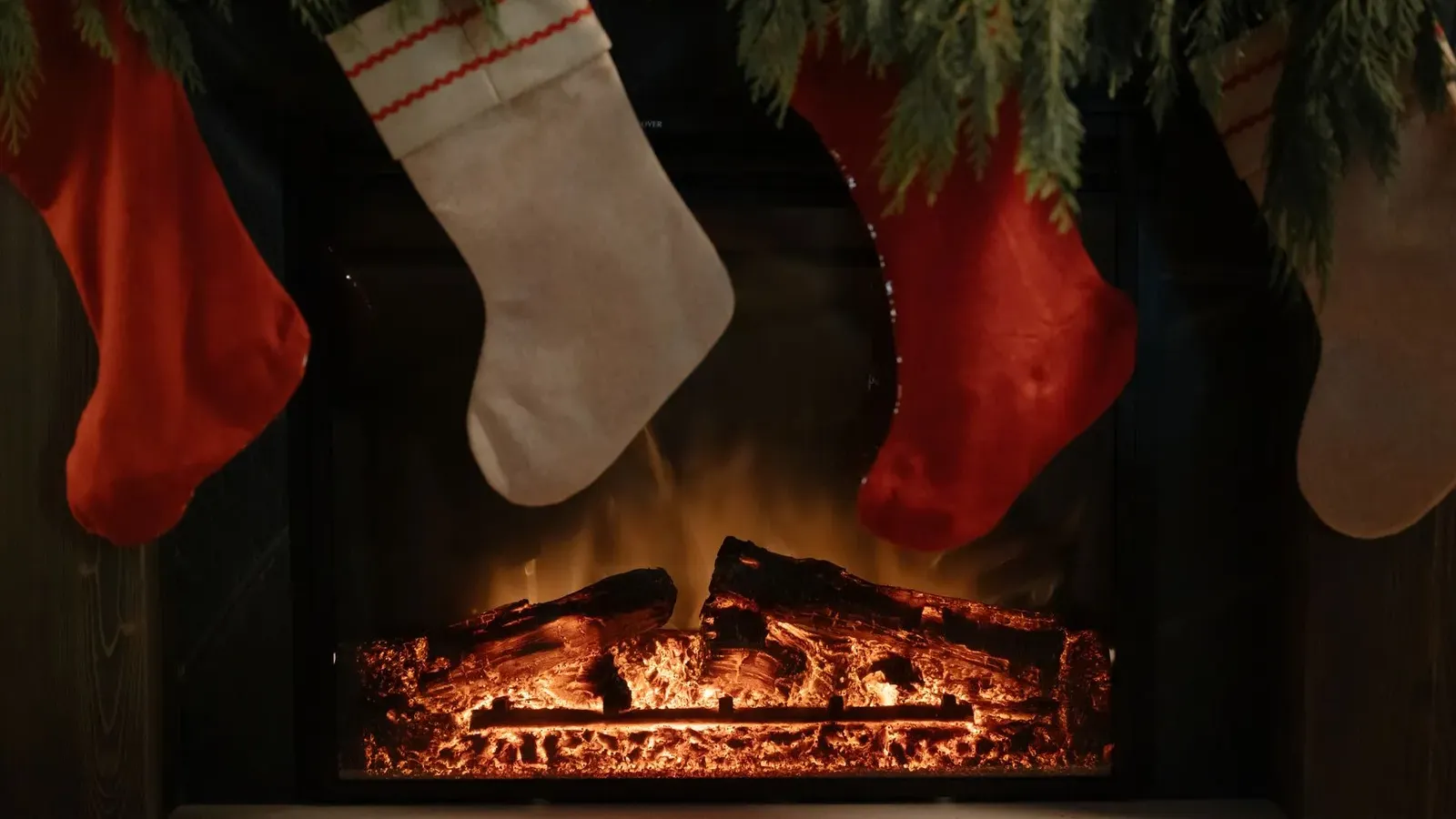 Red and cream linen stockings hanging above a glowing log fire beneath a fir garland