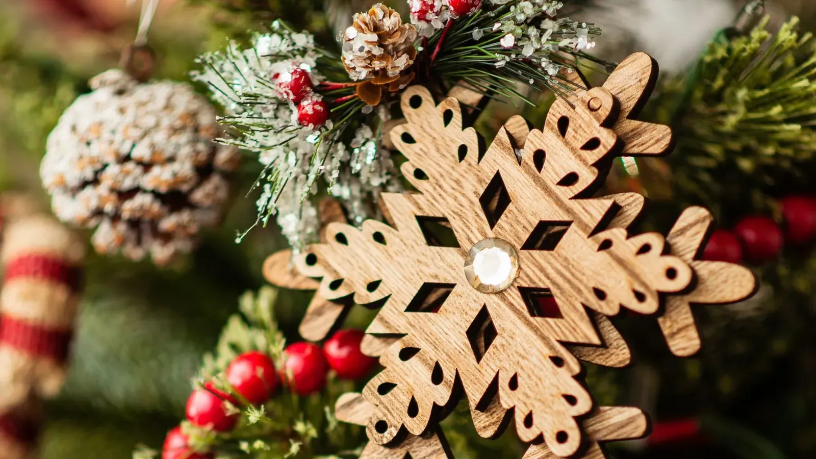 Carved wooden snowflake ornament with frosted pine cones and a red bead garland on a green Christmas tree