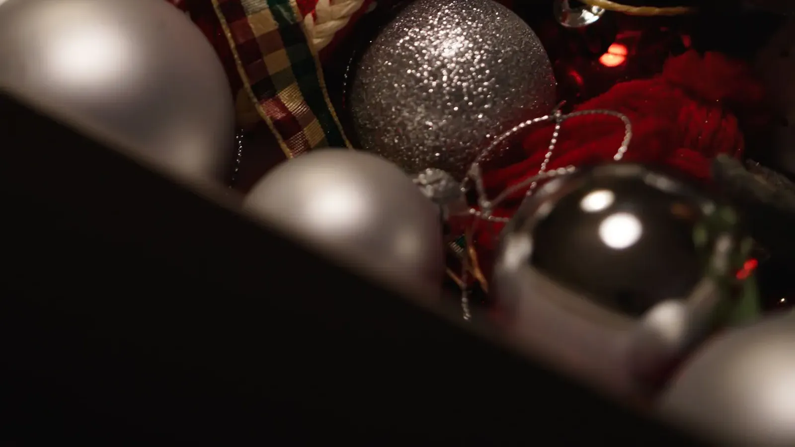 Box packed with silver glitter baubles and a knitted red and white ornament, in low light