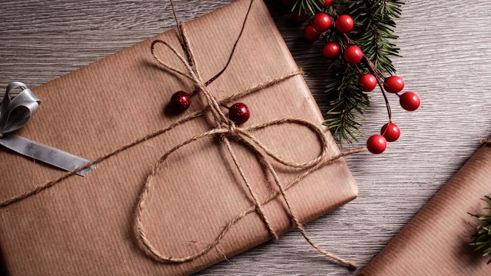 Present wrapped in brown paper and twine with red berries and a fir sprig on a grey wooden table