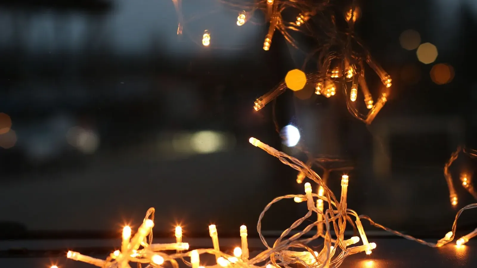 Tangle of warm white fairy lights glowing on a dark ledge, with a dusky blurred outdoor scene behind