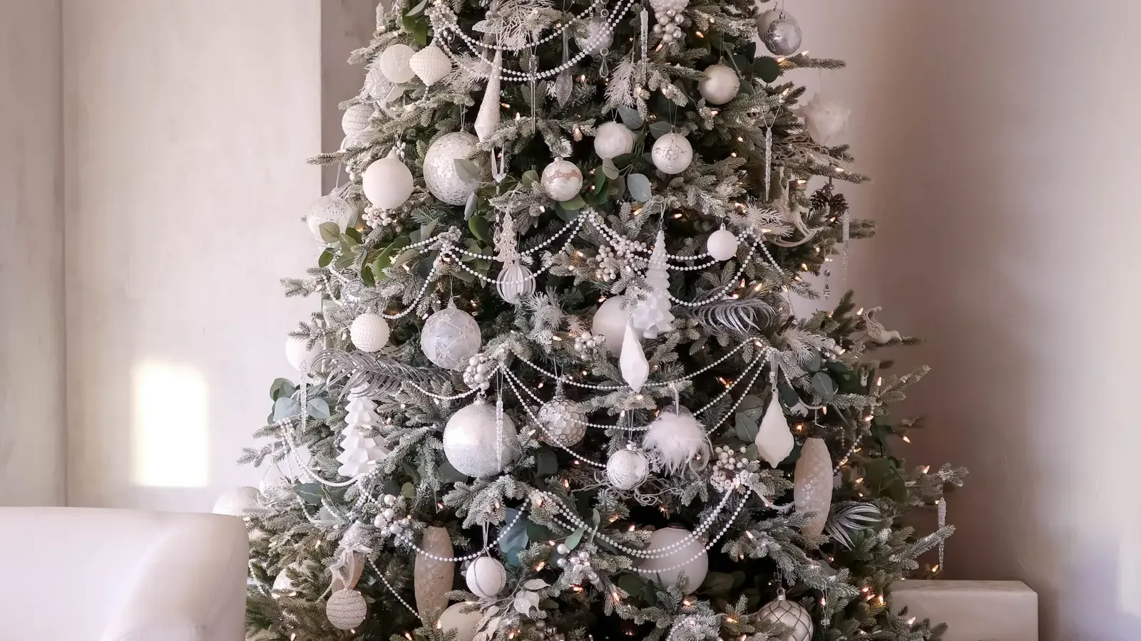 Tree decorated in white and silver with pale wrapped gifts, a white rocking horse and a fluffy pouffe