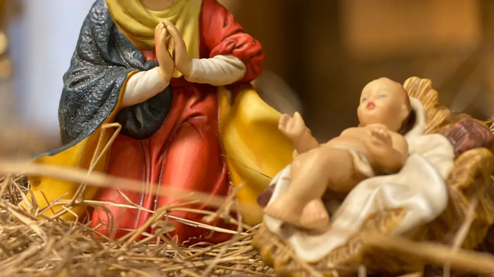 Close-up of a painted figurine of Mary praying beside a baby Jesus figure in a straw-filled manger