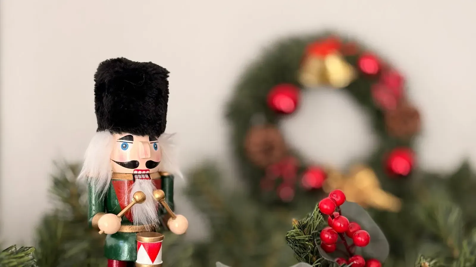 Guardsman nutcracker in a black bearskin hat standing among fir greenery and red berries, wreath blurred behind