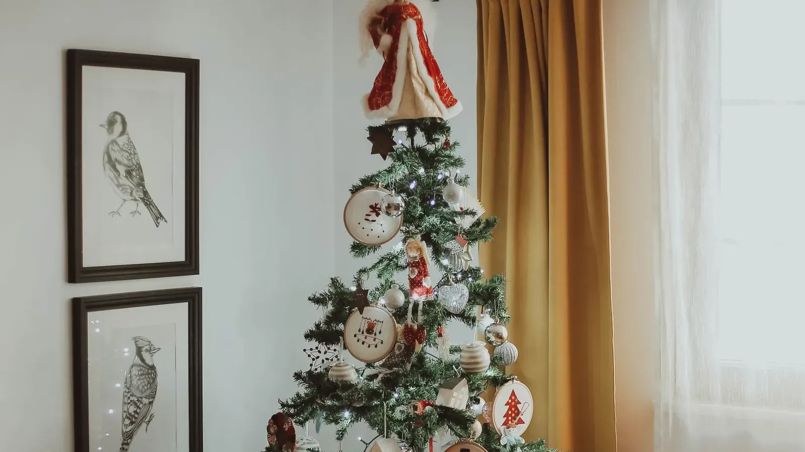 Christmas tree with handmade ornaments on a tartan skirt, two Santa figures and framed bird prints in a cosy room