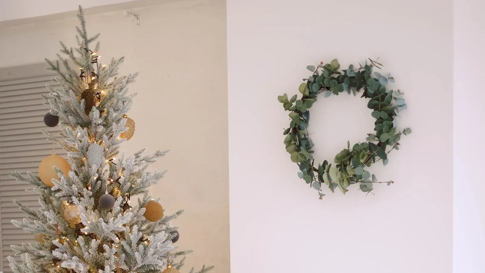 Frosted Christmas tree with soft gold baubles in a white corner with a green wreath, log niche and knitted blanket